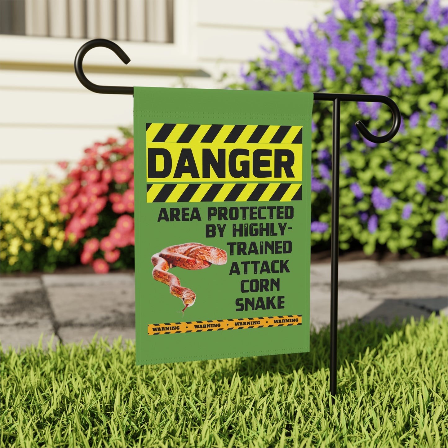 A green flag with a yellow and black warning sign attached to it, indicating a danger zone protected by highly trained attack corn snake.