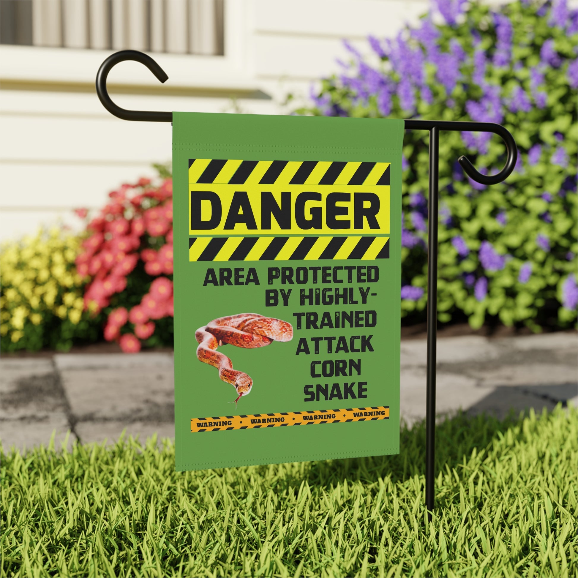 A green flag with a yellow and black warning sign attached to it, indicating a danger zone protected by highly trained attack corn snake.