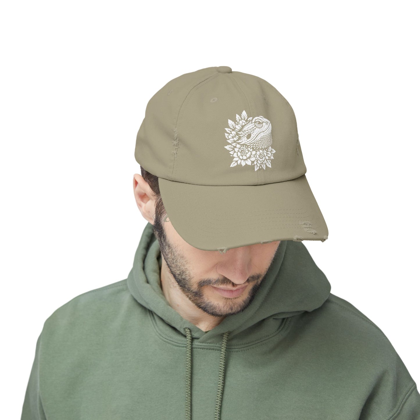 A man wearing a beige cap with a white floral design on it, along with a green hoodie.