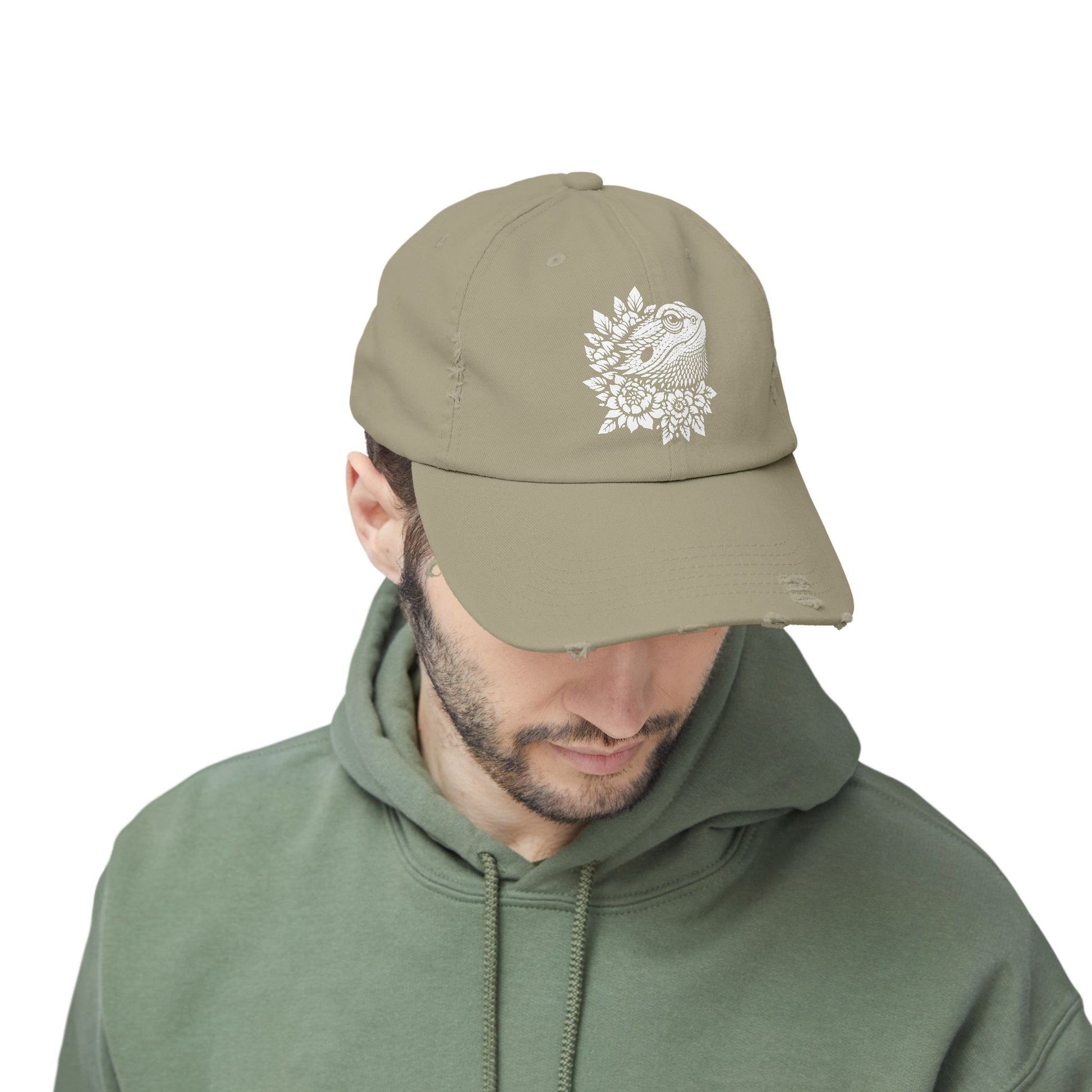A man wearing a beige cap with a white floral design on it, along with a green hoodie.